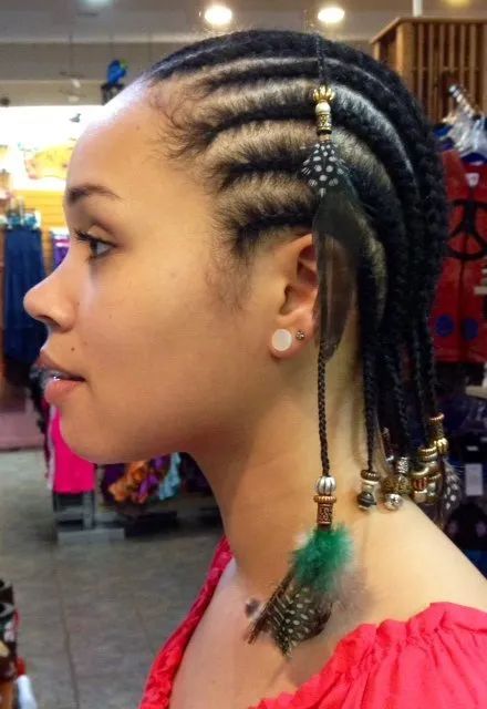 Profile view of a woman with cornrow braids and beaded hair accessories, wearing a red off-shoulder top.