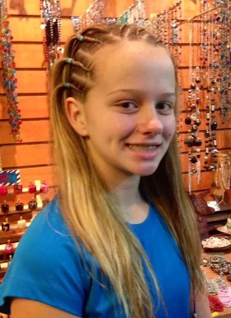 Smiling girl with braided blonde hair in a blue shirt, standing in a jewelry shop.