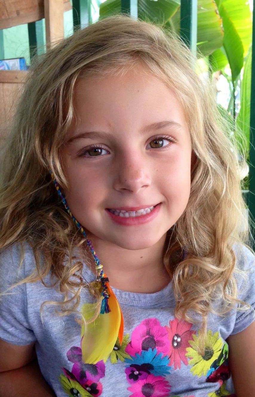 Smiling child with curly blonde hair wearing a gray shirt with colorful flowers