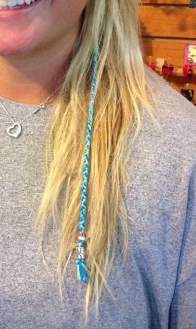 Close-up of a person wearing a gray shirt and necklace, with long blonde hair and a turquoise pendant.