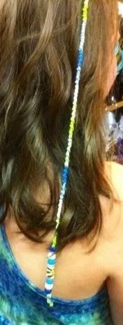 Back of a person with long brown hair and a blue beaded braid accent, wearing a teal top