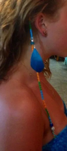 Close-up of a woman wearing a bright blue teardrop earring and colorful beaded necklace.