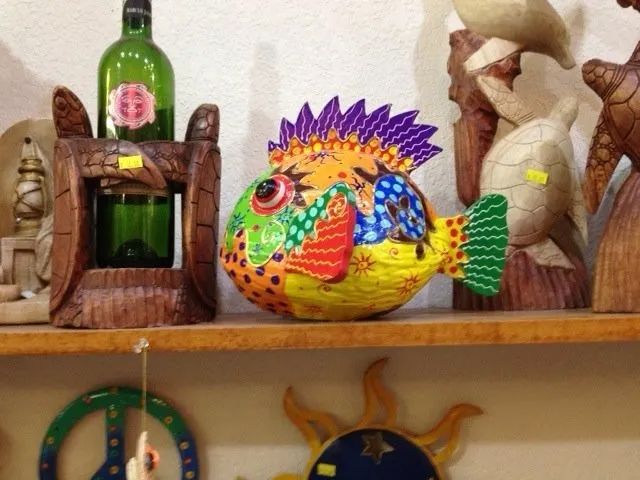 Colorful hand-painted fish figurine on a shelf, with decorative bottles and ceramic items in the background