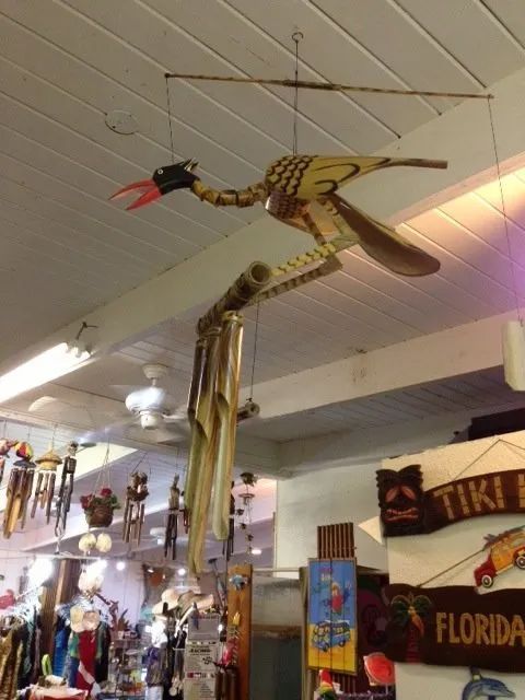 Colorful hanging bird sculpture in a tiki-style shop with Florida souvenirs and decor.