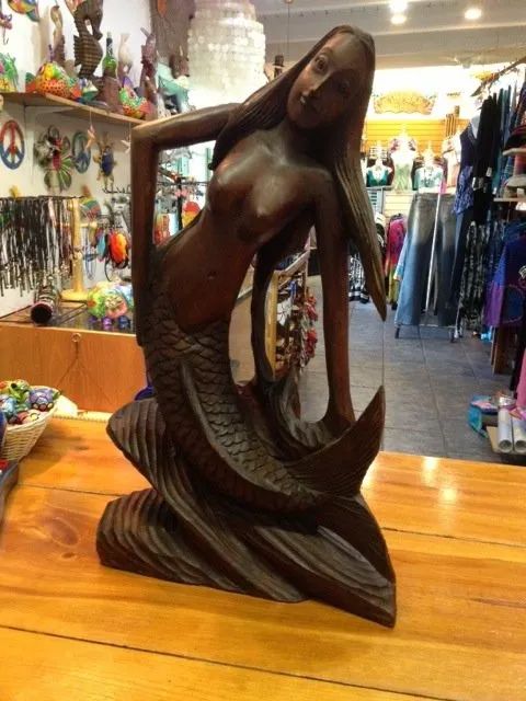 Dark wooden mermaid sculpture displayed on a wooden table in a gift shop.