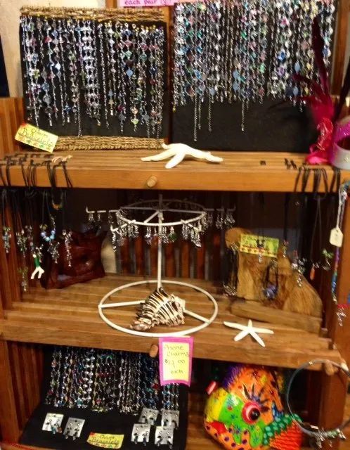 Display of colorful beaded jewelry and shell necklaces on wooden shelves at a market stall