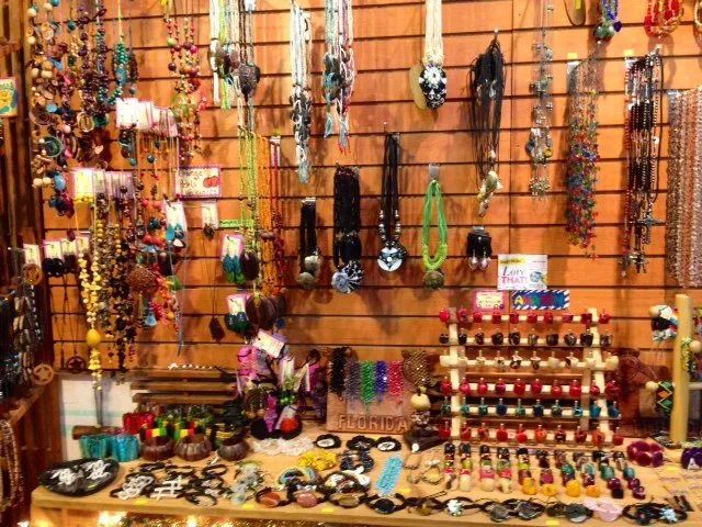Jewelry stall with colorful necklaces, bracelets, and trinkets displayed on a wooden wall and table.