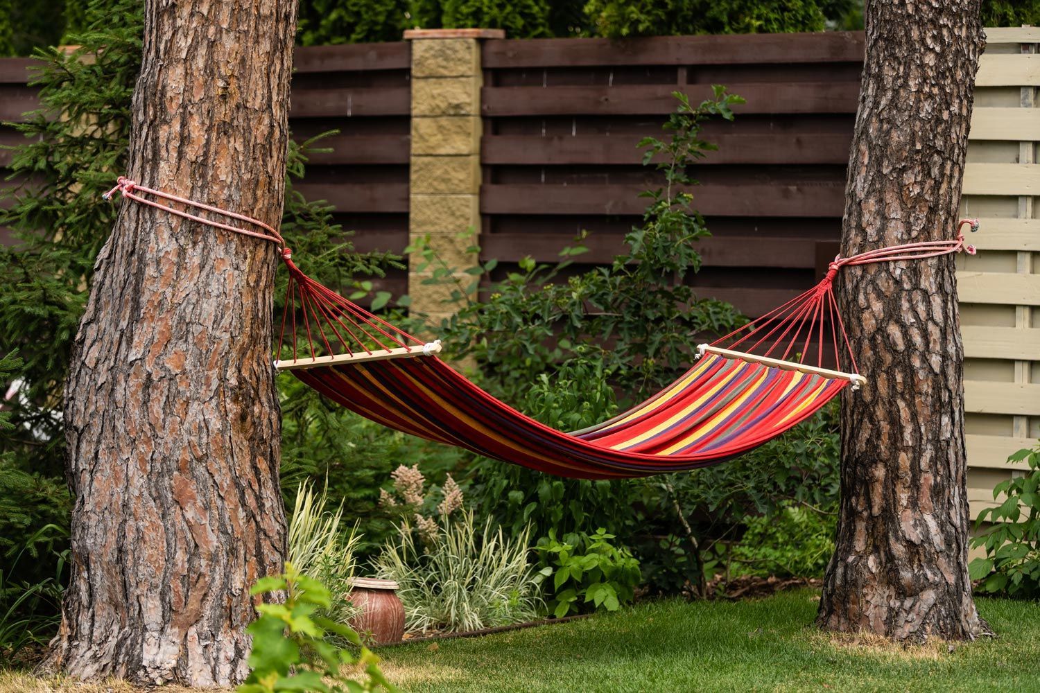 Red striped hammock hanging between two trees in a garden lawn