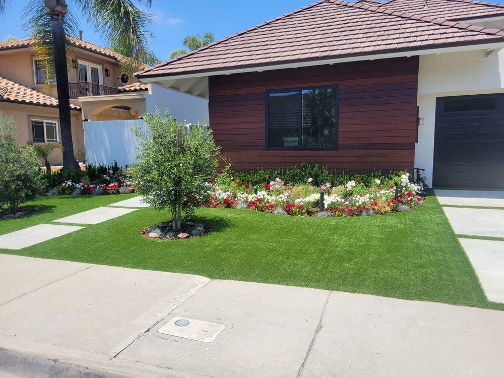 Modern house with manicured lawn, flower bed, and palm tree beside a driveway