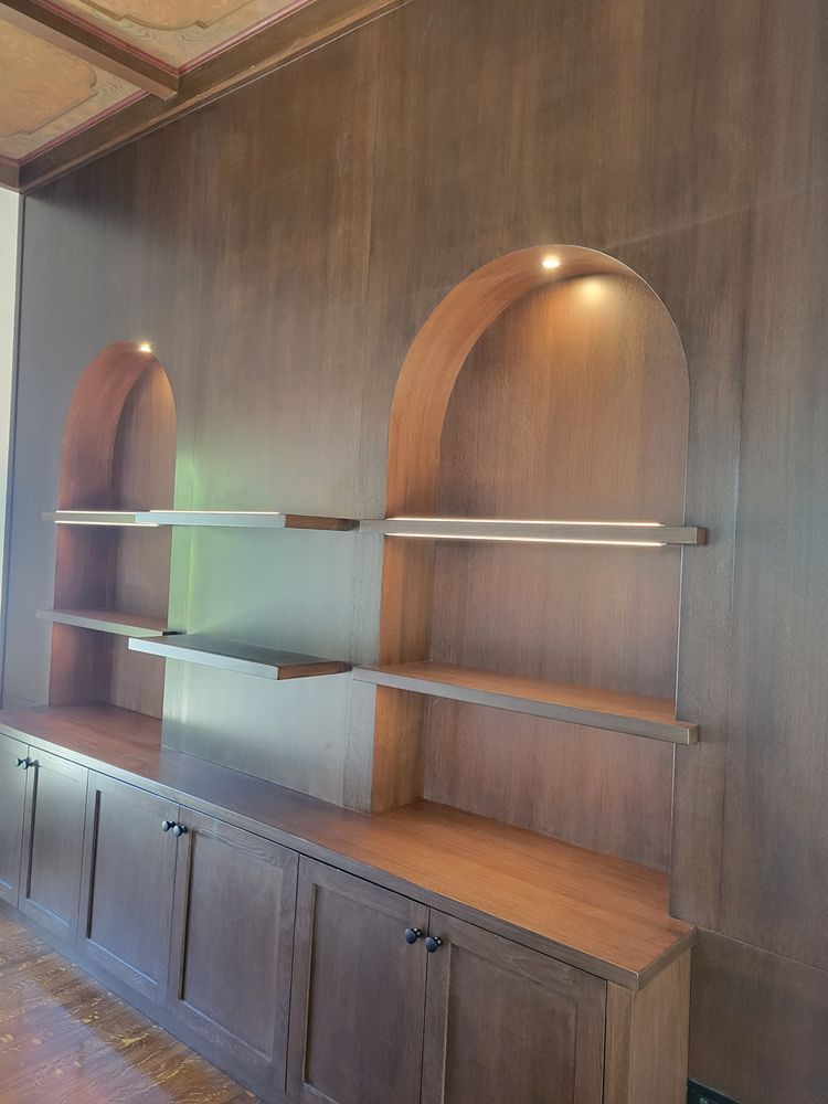 Built-in wooden shelving with arched niches and cabinet storage in a paneled room