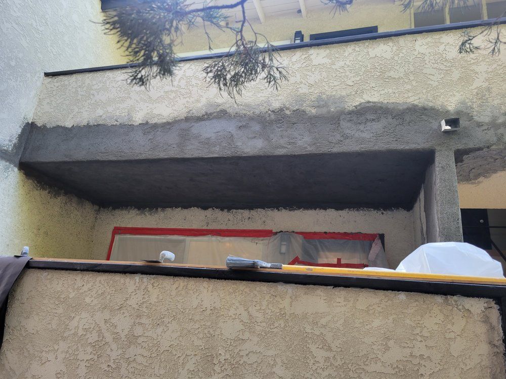Building balcony with concrete overhang and red-trimmed window, viewed from below