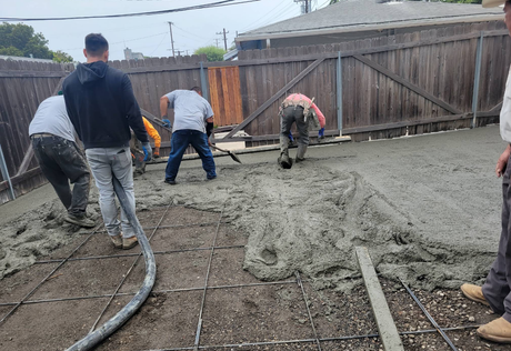 Workers spreading wet concrete in a backyard near a wooden fence