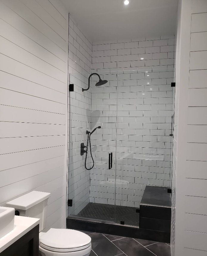 Modern white-tiled bathroom with a walk-in shower, handheld showerhead, and toilet in the foreground