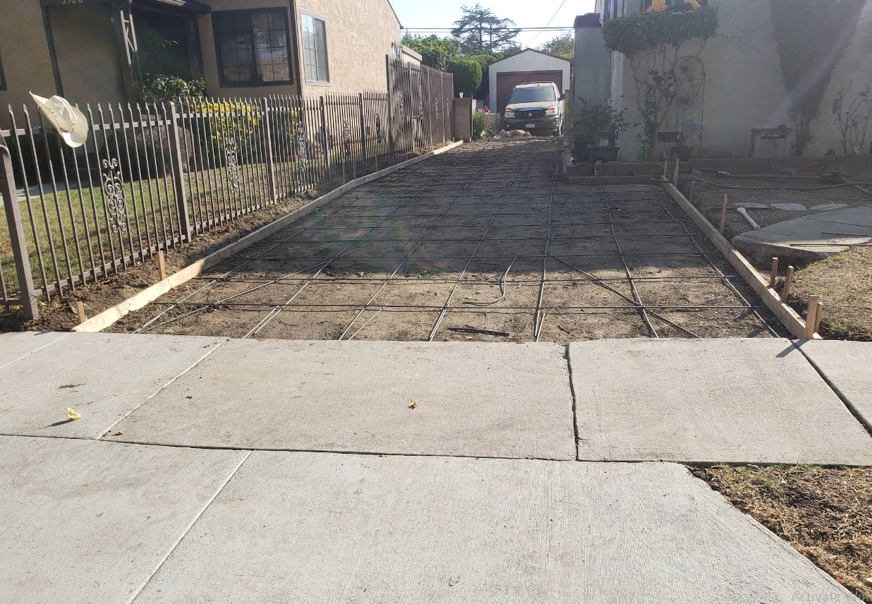 Damaged driveway with cracked concrete and a rough dirt strip leading to a gate and house