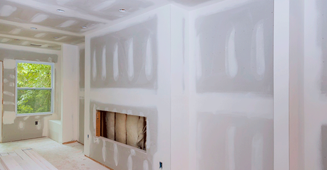 Bright unfinished room with drywall, a window, and a recessed fireplace opening