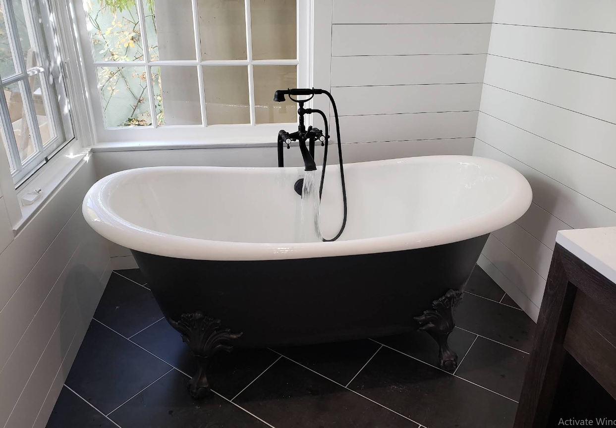 Clawfoot bathtub with black exterior and chrome faucet in a bright tiled bathroom