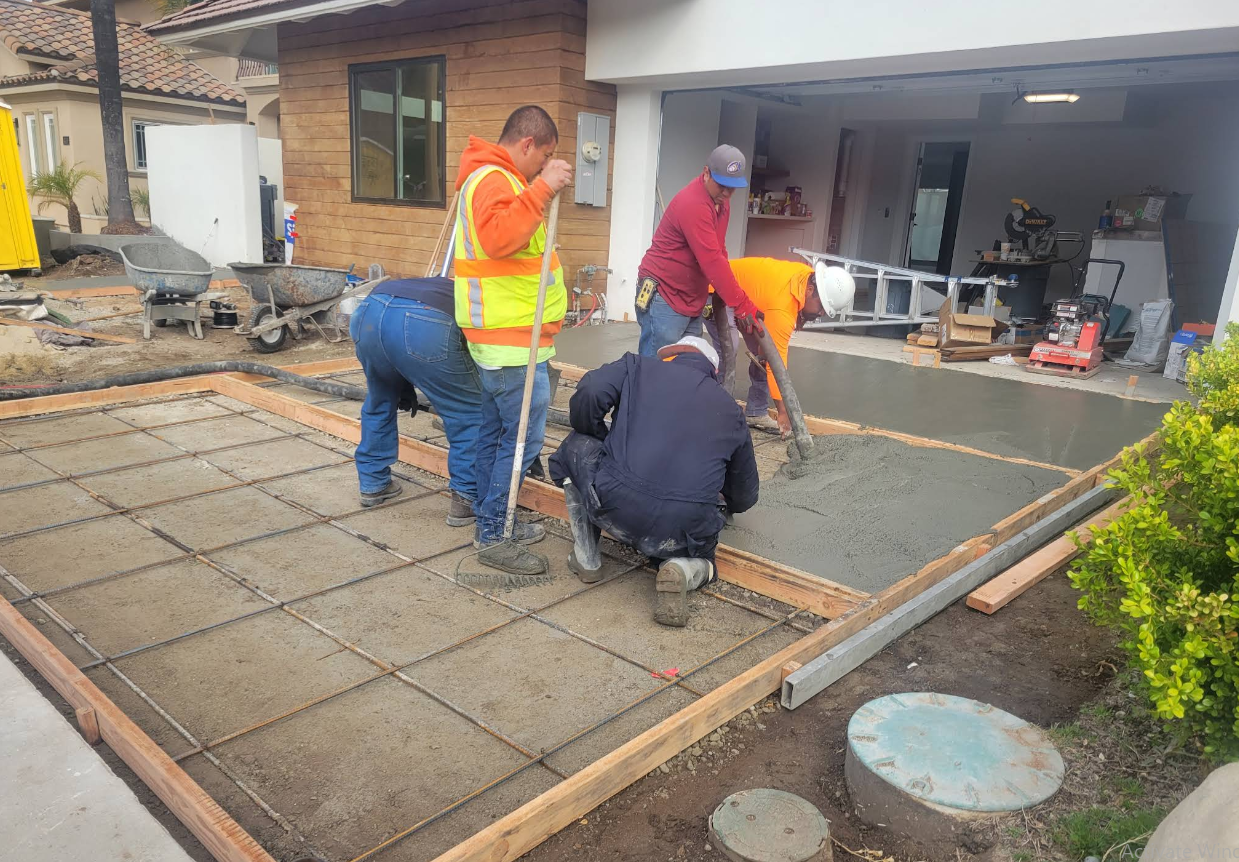 Workers pouring and smoothing concrete in a driveway beside a house and garage.