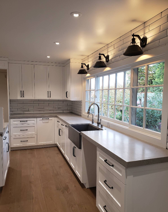 Bright modern kitchen with white cabinets, long countertop, and large window over the sink.
