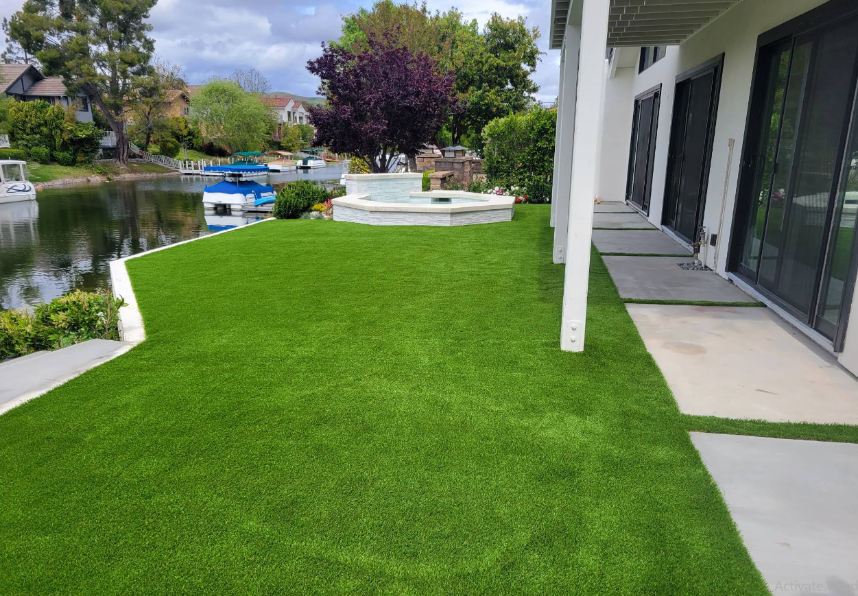 Green lawn beside a modern house with a canal, patio, and trees in the background