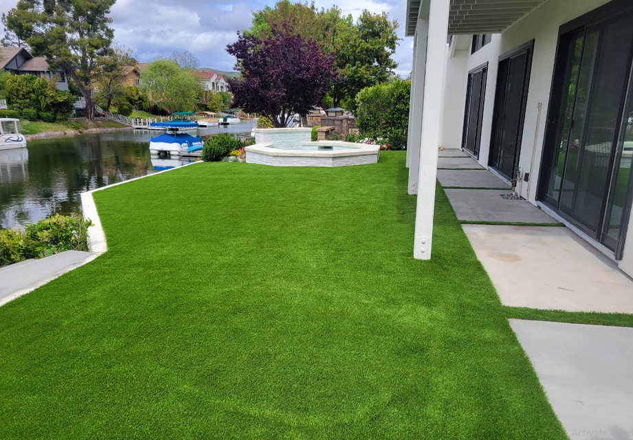 Backyard patio with bright green lawn, pond, and modern house exterior under cloudy sky