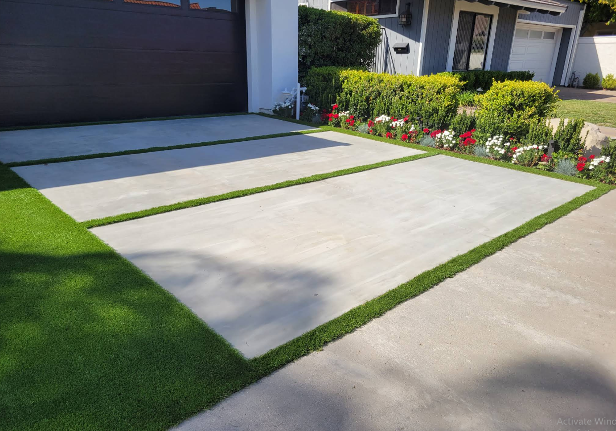 Modern suburban driveway with clean concrete slabs, green lawn, and front garden by a garage