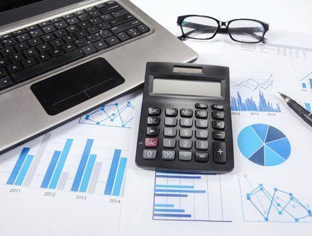 A calculator is sitting on top of a laptop next to a pen and glasses.