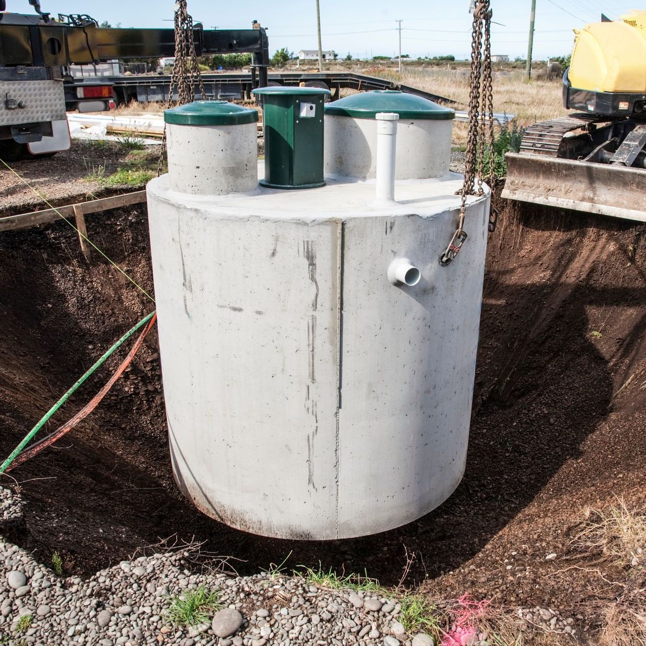 A large concrete cylinder is being lifted into the ground