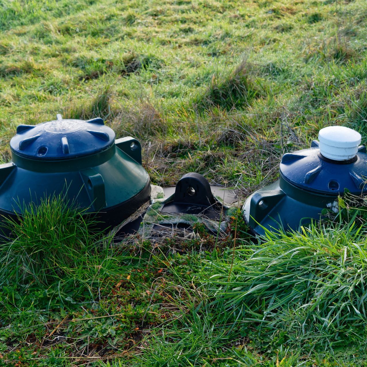 Two green containers are sitting in the grass in a field.
