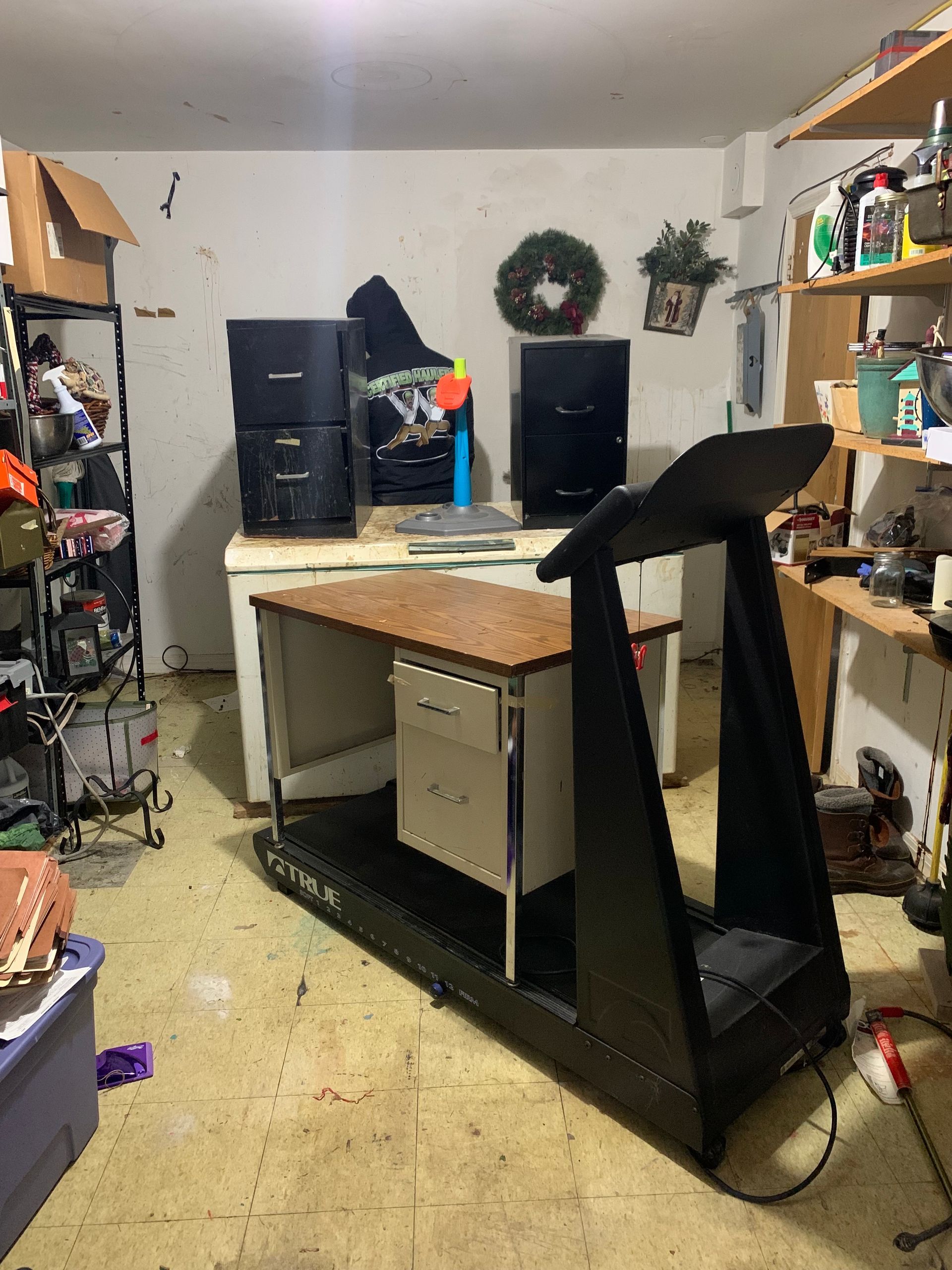 Treadmill desk in a cluttered garage, with filing cabinets and a shelf of items visible.