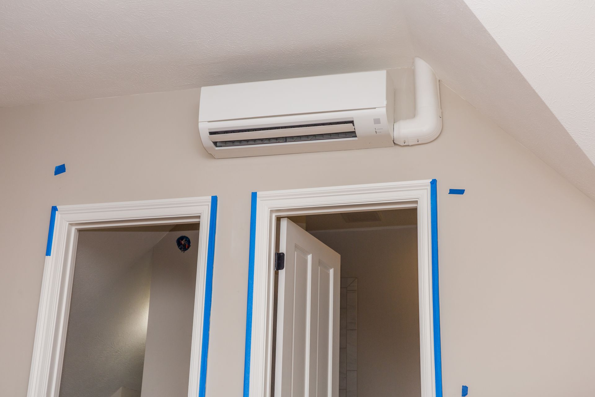 Interior doorway with blue painter’s tape around trim and a wall-mounted air conditioner above.