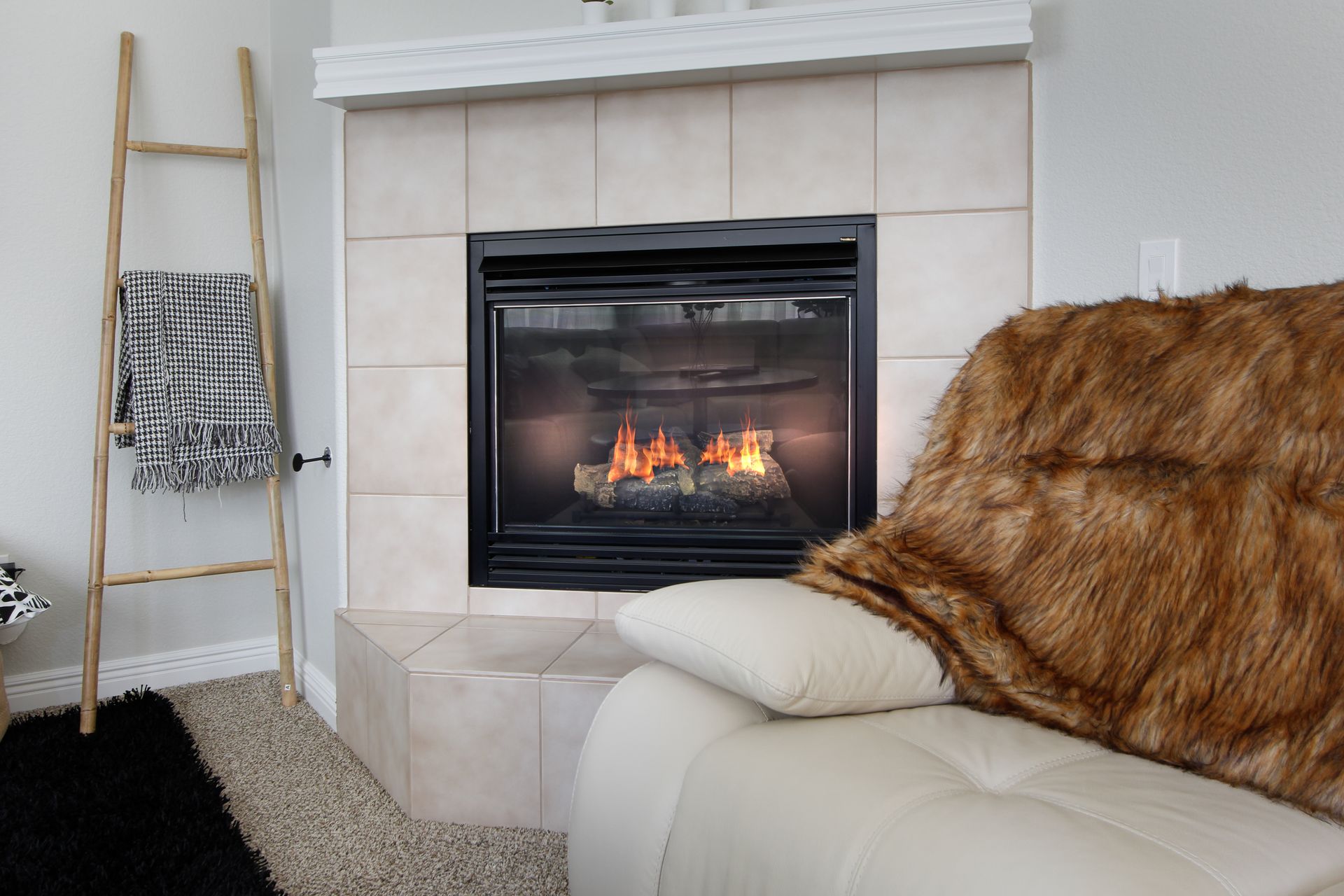 Modern living room with lit fireplace, beige tile surround, cream sofa, and fur throw blanket