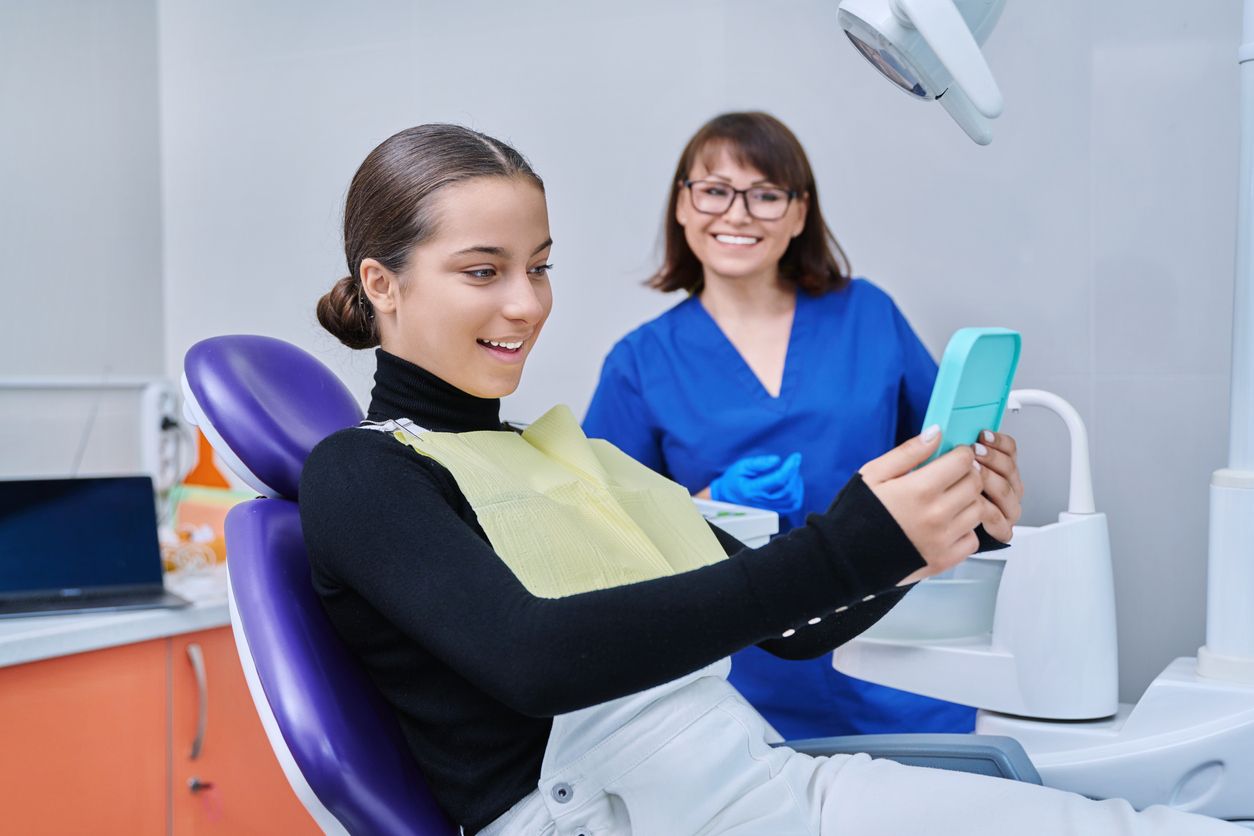 A woman is sitting in a dental chair looking at her phone.