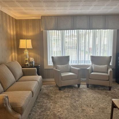 Living room with sofa, two armchairs, and a large window with sheer curtains.