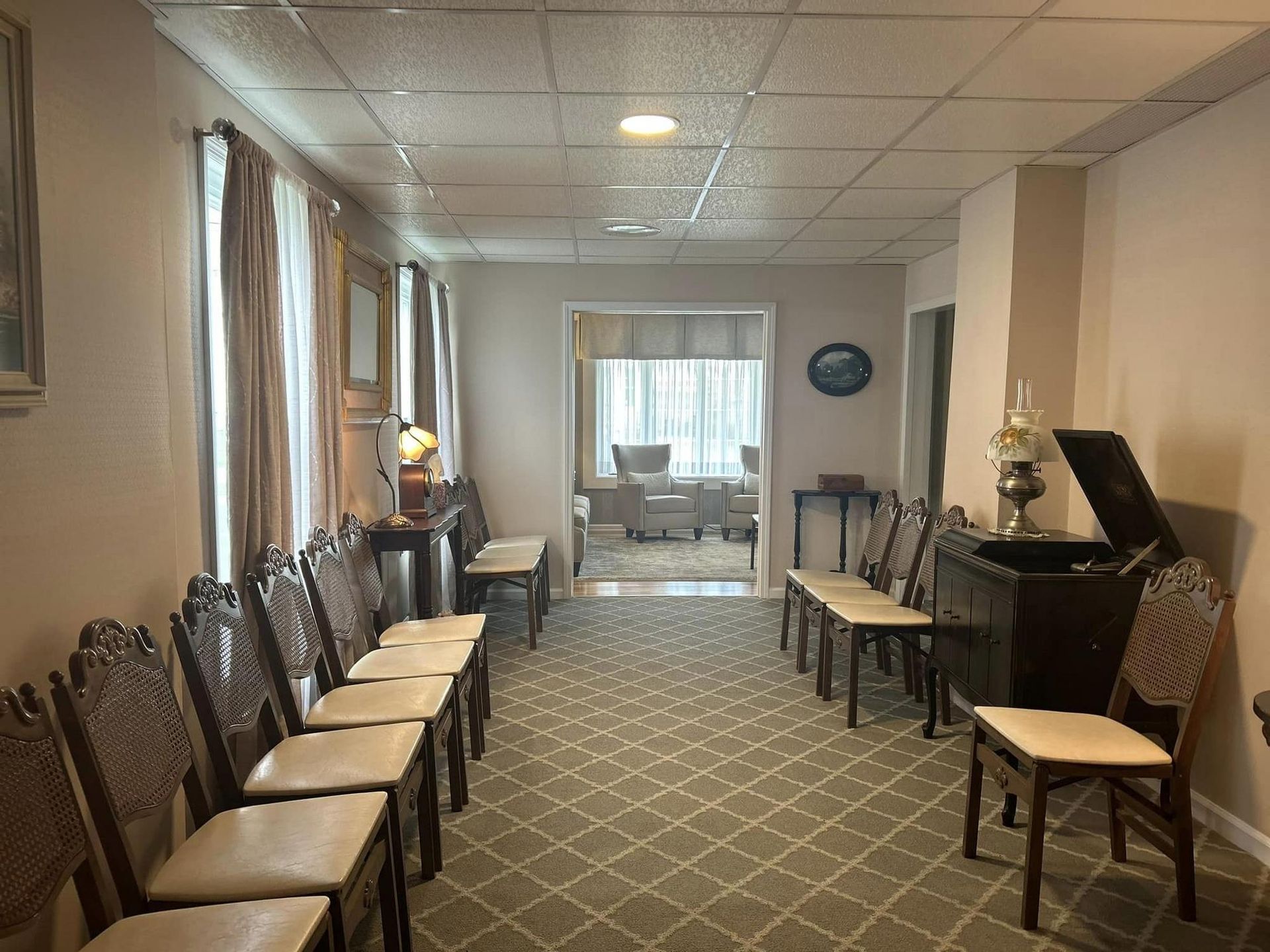 Hallway with chairs. Light-colored walls, patterned carpet. Entrance to another room visible.