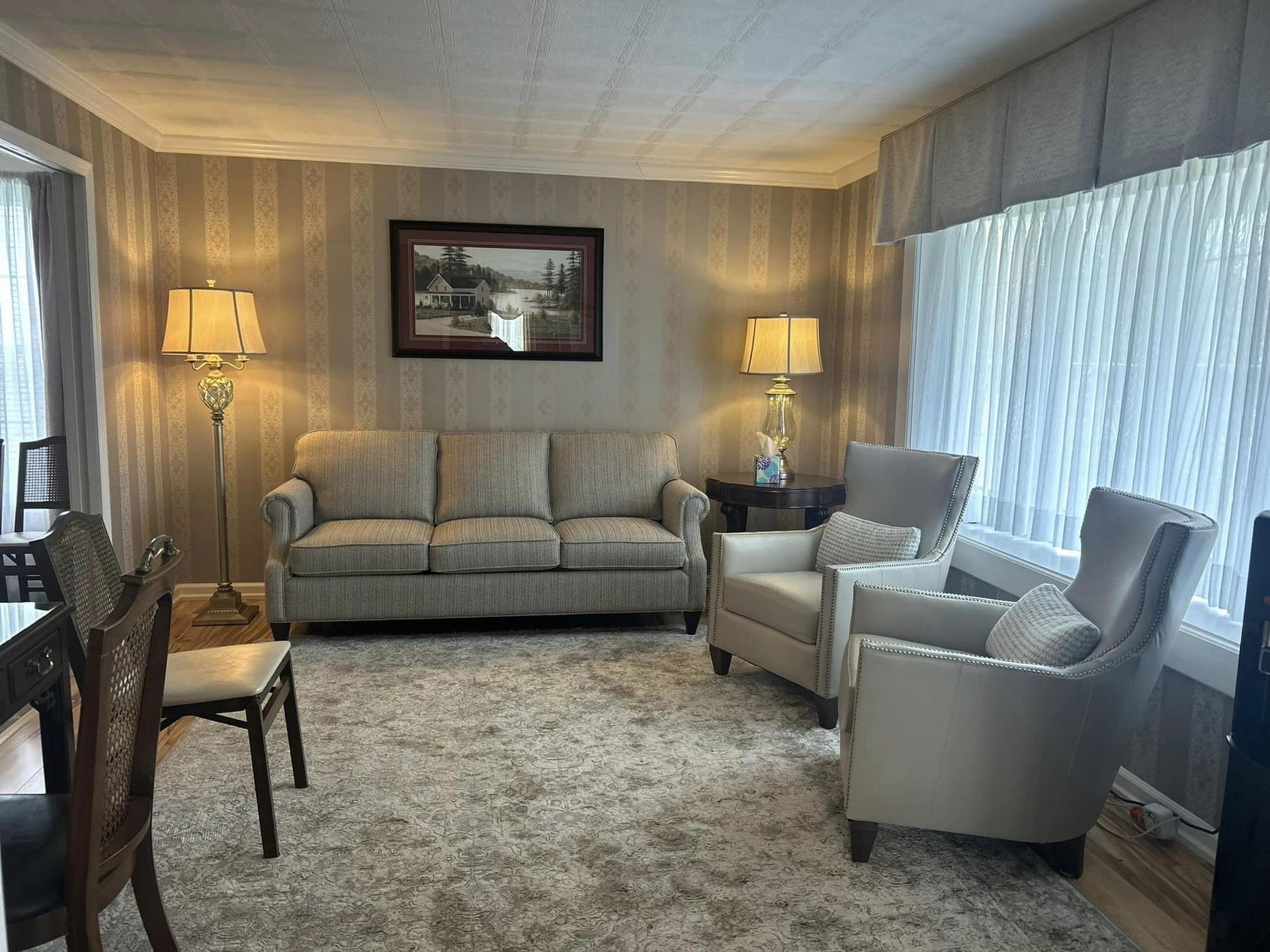 Living room with sofa, two armchairs, lamps, and a window; neutral color scheme.