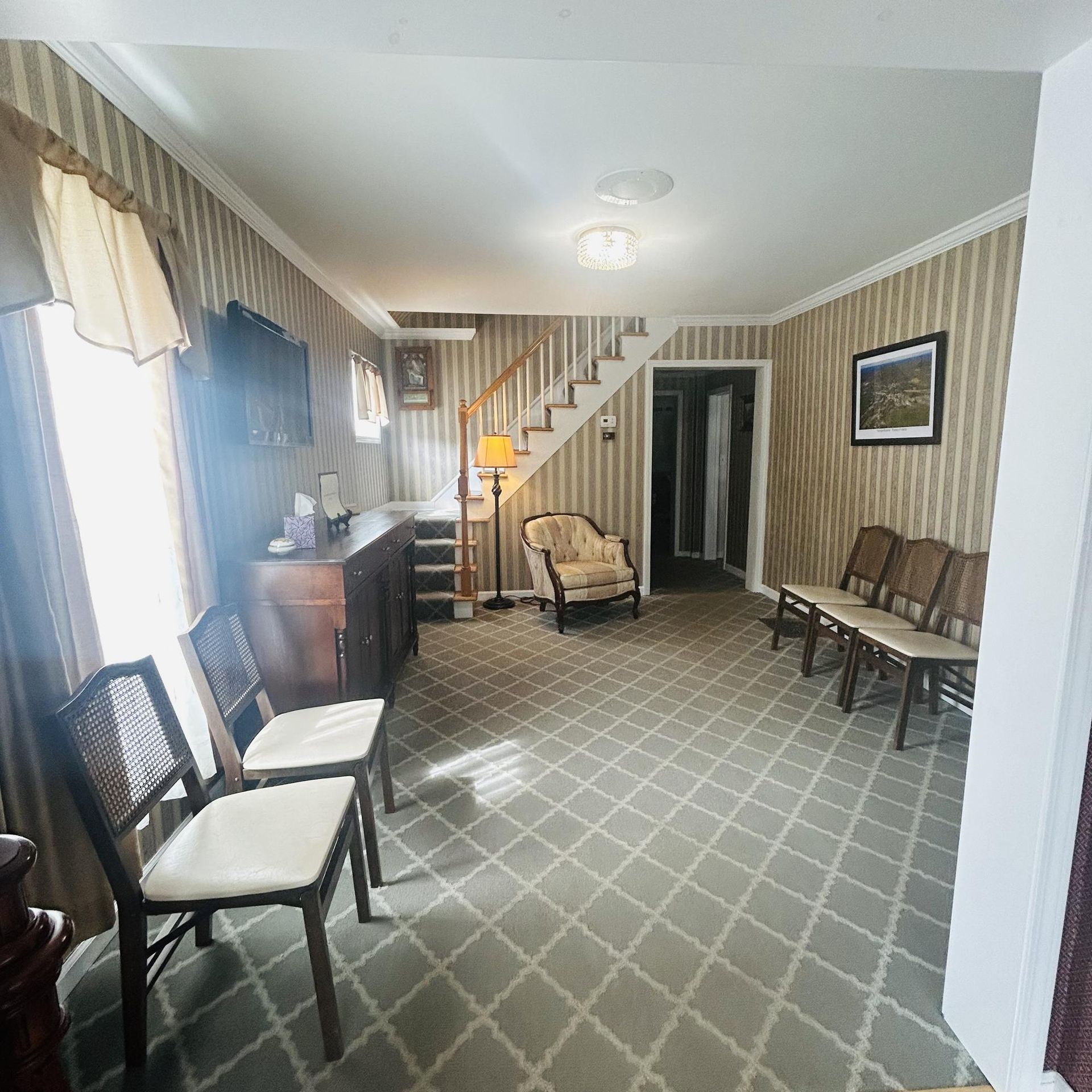 A room with patterned wallpaper, chairs, and a staircase.