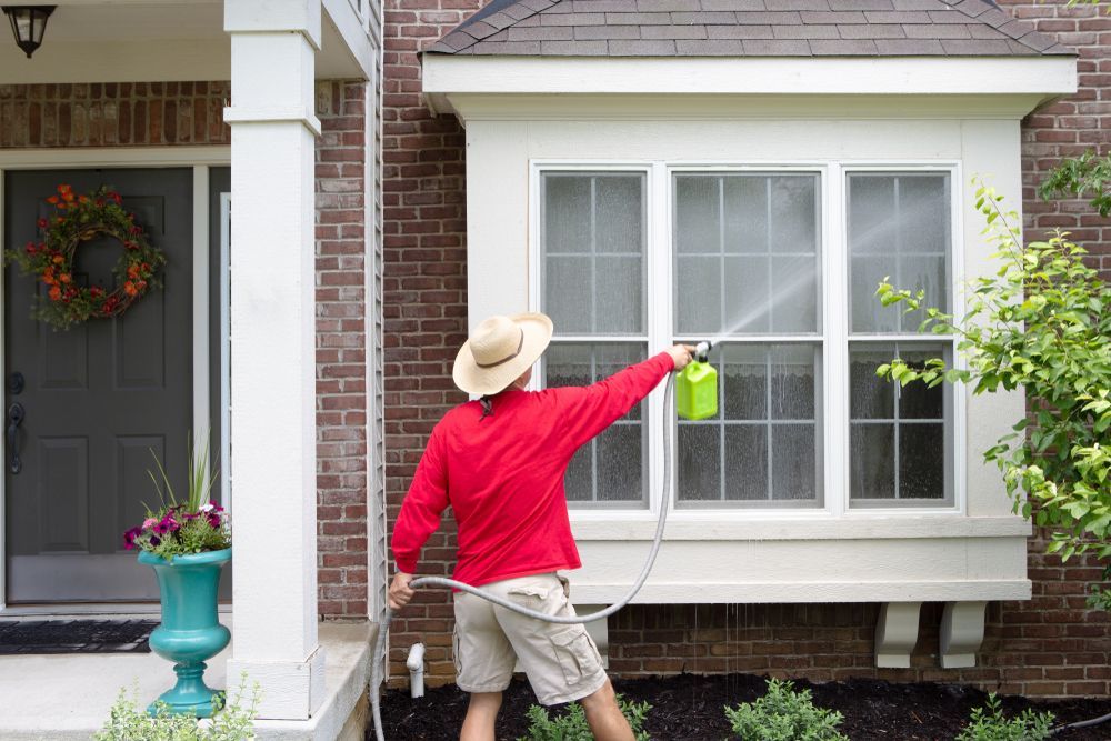 Person in Red Shirt and Hat Using a Hose Sprayer to Wash the Exterior Windows — A1 Roof Cleaning In Kepnock, QLD