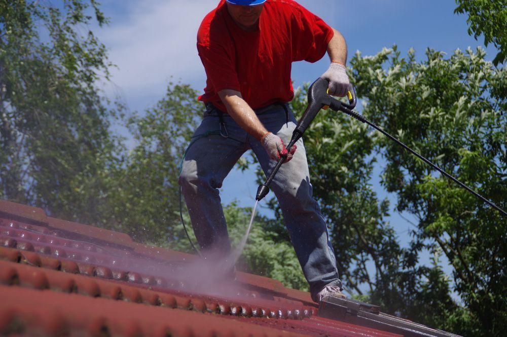 Worker Pressure-washing a Red Roof, Wearing a Red Shirt and Jeans — A1 Roof Cleaning In Hervey Bay, QLD