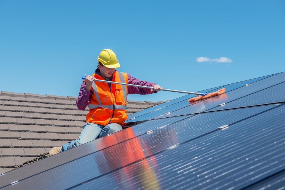 Worker in Orange Safety Vest Cleaning Rooftop Solar Panels With a Squeegee — A1 Roof Cleaning In Kepnock, QLD