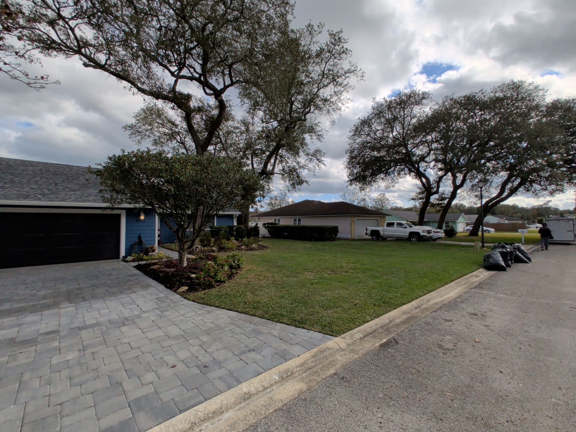 A residential street with houses, trees, and a parked white pickup truck on a cloudy day.