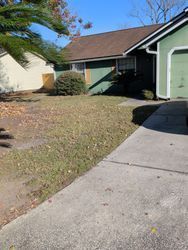 Green house with brown roof and concrete driveway. Sparse grass yard.