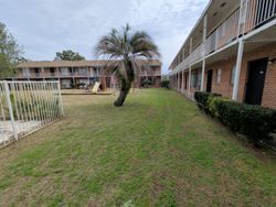 Apartment buildings with a grassy courtyard, palm tree, and a small playground on an overcast day.