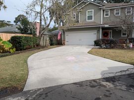 House with a concrete driveway, two-car garage, and green siding. Grass and bushes flank the driveway.