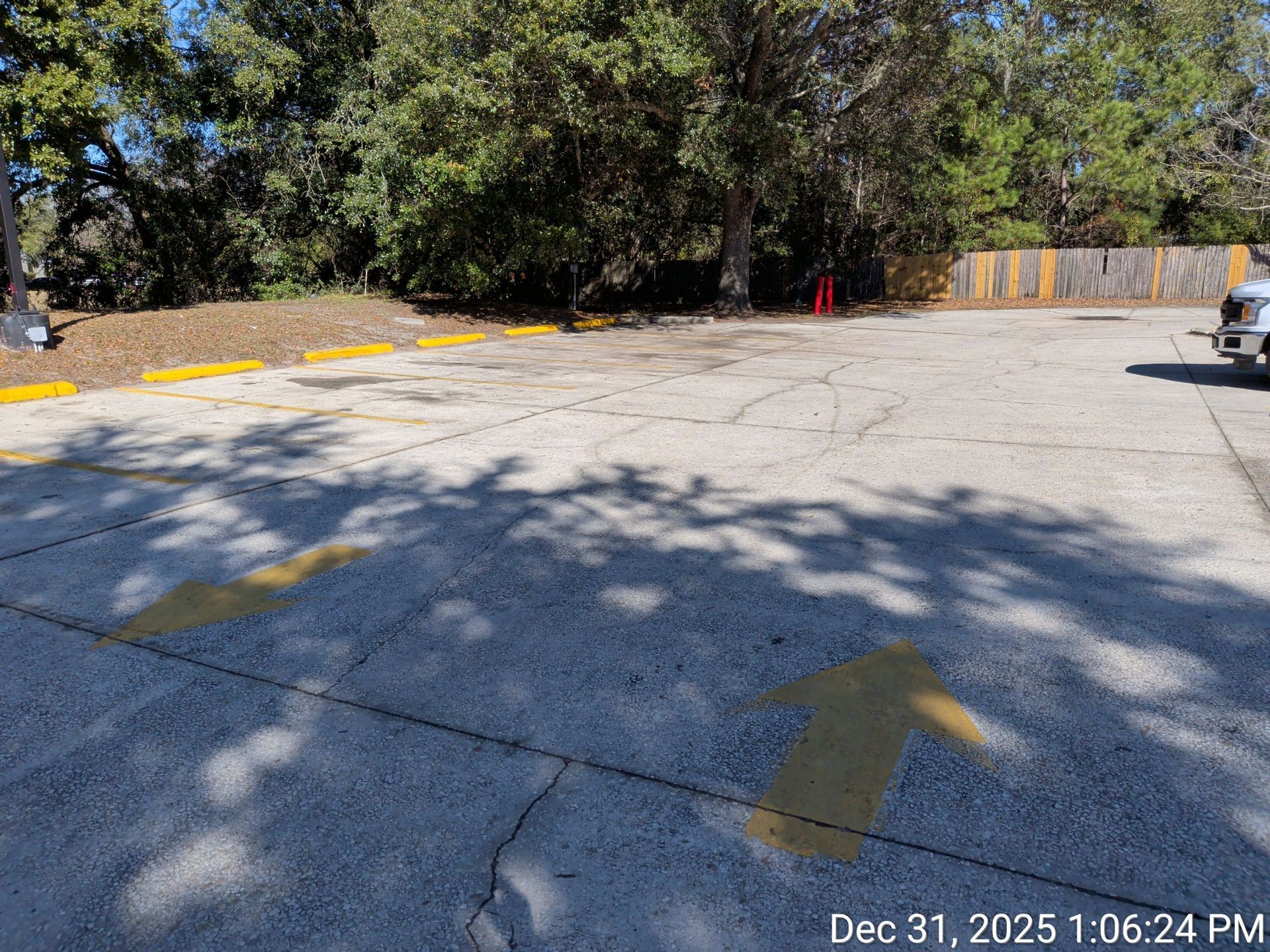 Parking lot with yellow arrows and curb stops, trees in the background, and a vehicle on the right.