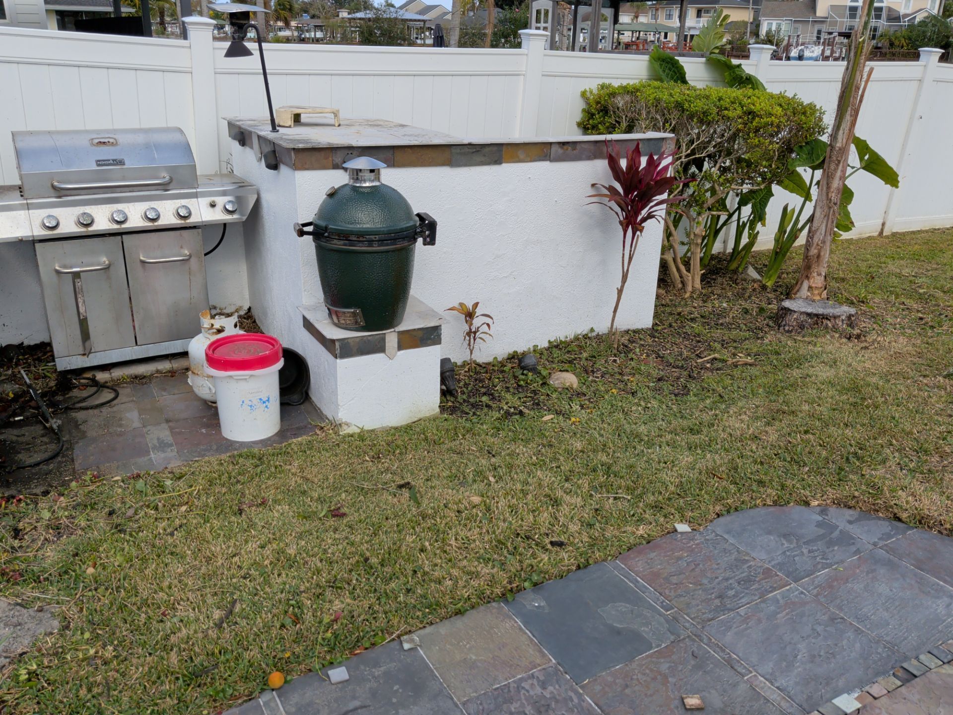 Backyard grilling area with a grill, Big Green Egg, propane tank, and white stucco structure.