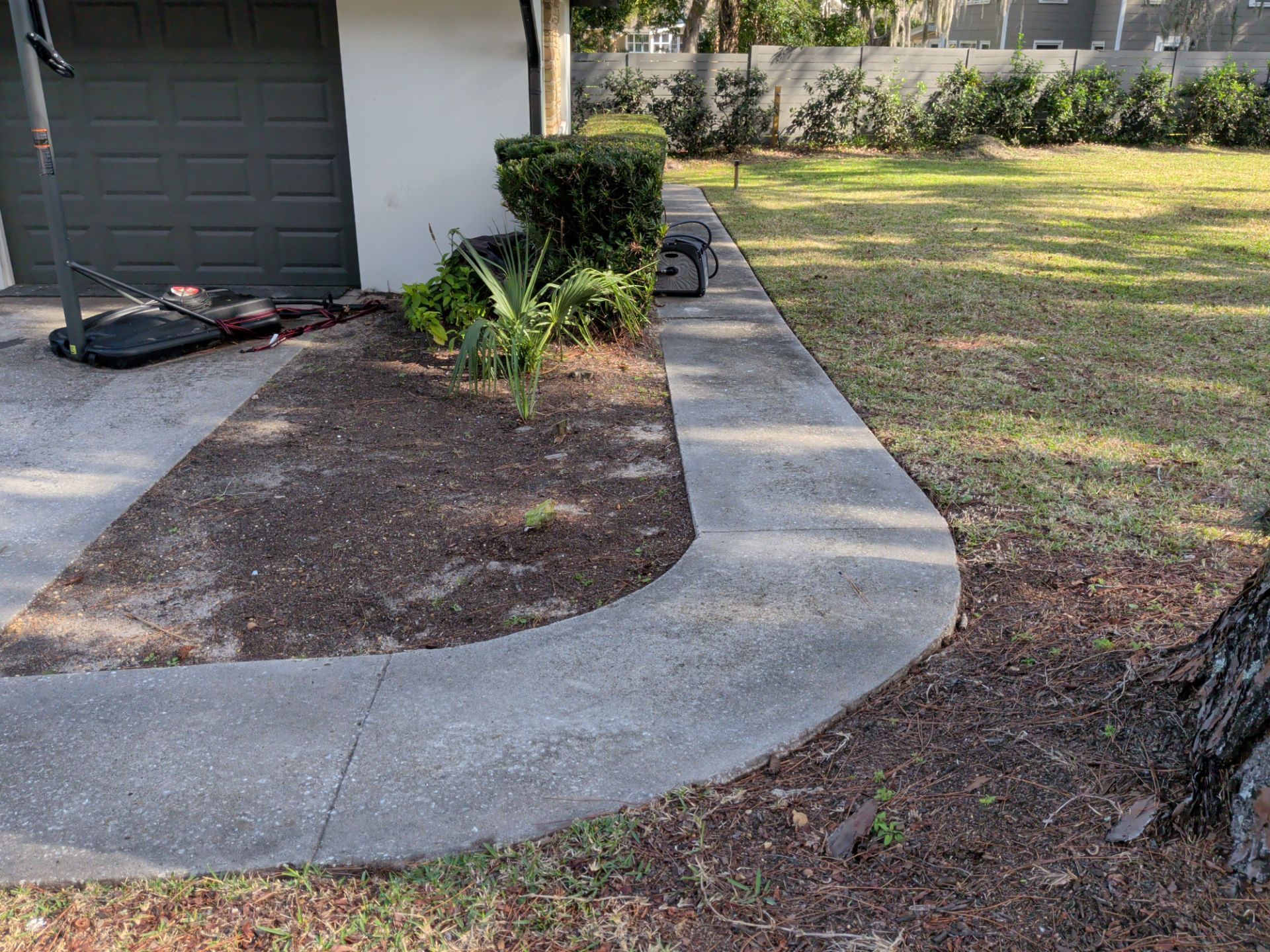 A concrete pathway curves in front of a house, with a small garden bed and a green lawn.