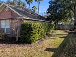 A brick house with trimmed green hedges along a side yard. Brown grass.