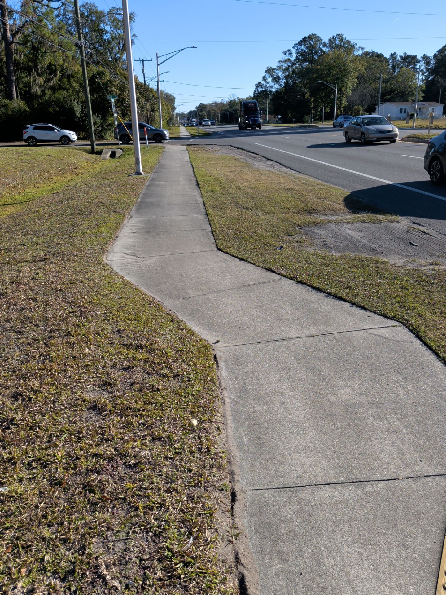 Sidewalk with angled turns alongside a road. Cars and trees are in the background.