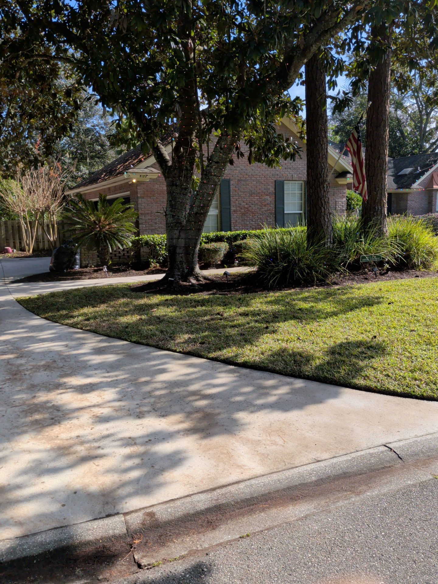 House with brick facade, trees, green lawn, and concrete sidewalk.