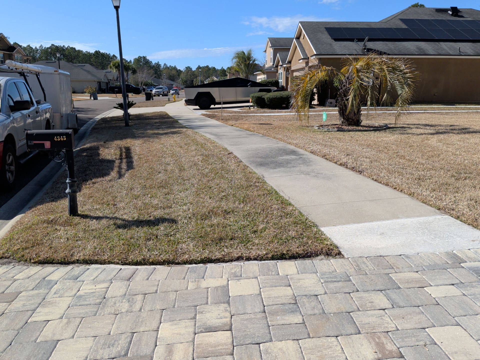 Sidewalk bordered by brick and dry grass in front of houses on a sunny day.